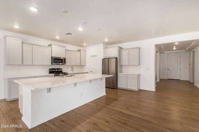 kitchen with appliances with stainless steel finishes, an island with sink, wood finished floors, and visible vents