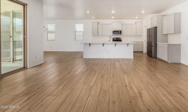 kitchen with light wood-style flooring, appliances with stainless steel finishes, a breakfast bar area, open floor plan, and light countertops