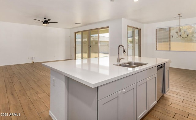 kitchen featuring light wood-style flooring, decorative light fixtures, a sink, light countertops, and stainless steel dishwasher