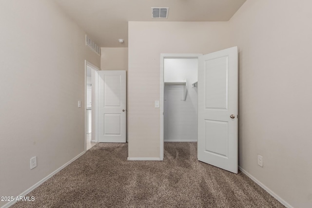 unfurnished bedroom featuring a closet, a walk in closet, carpet, baseboards, and visible vents