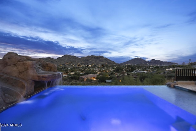 pool at dusk with pool water feature and a mountain view