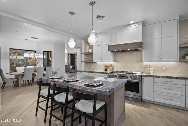 kitchen featuring high end range, a kitchen bar, light wood-type flooring, pendant lighting, and white cabinets