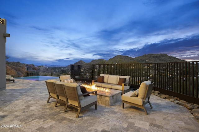 patio terrace at dusk featuring an outdoor living space with a fire pit, pool water feature, a mountain view, and a fenced in pool