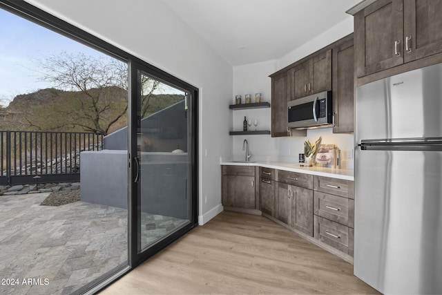 kitchen with sink, dark brown cabinets, light hardwood / wood-style floors, and appliances with stainless steel finishes