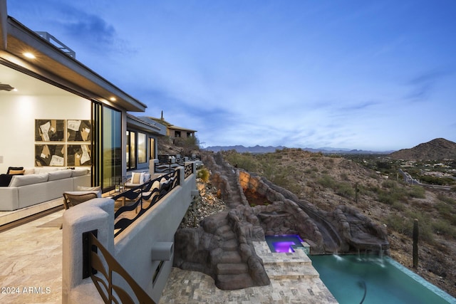 pool at dusk featuring a mountain view, pool water feature, a patio, and an outdoor hangout area