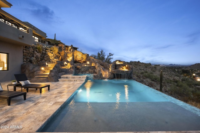 pool at dusk with a patio area and pool water feature