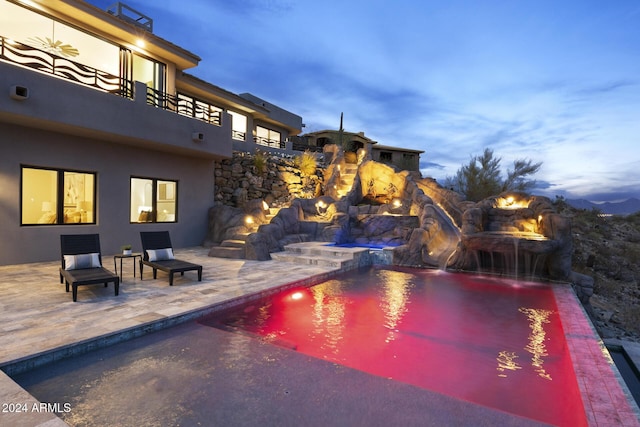 pool at dusk with pool water feature and a patio