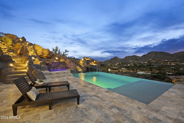 pool at dusk featuring pool water feature, a mountain view, and a patio area