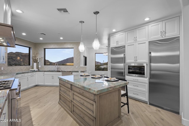 kitchen featuring built in appliances, pendant lighting, white cabinets, and light stone countertops