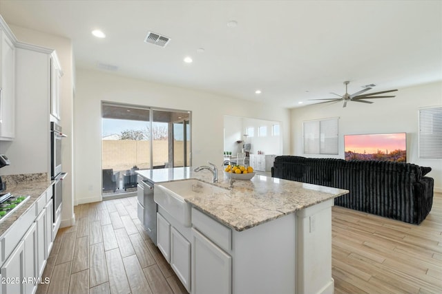 kitchen featuring sink, white cabinetry, light stone countertops, an island with sink, and light hardwood / wood-style floors