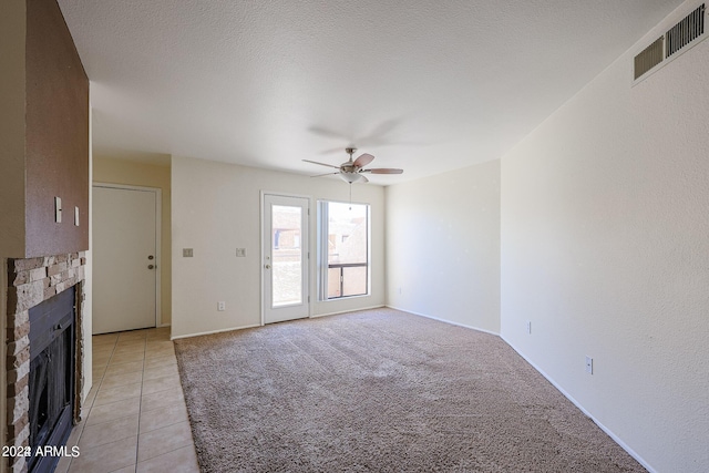 unfurnished living room featuring a textured ceiling, ceiling fan, light tile patterned floors, and a fireplace