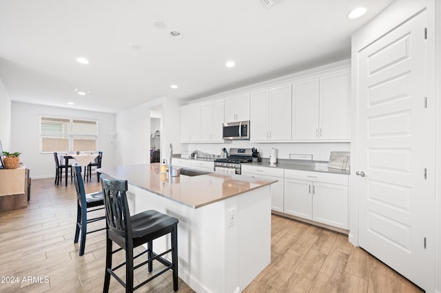 kitchen featuring white cabinets, stainless steel appliances, a center island with sink, and a breakfast bar area