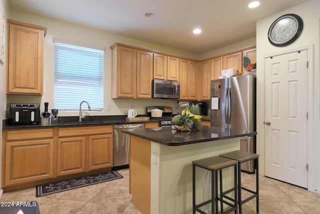 kitchen with sink, stainless steel appliances, light tile patterned floors, dark stone countertops, and a kitchen island