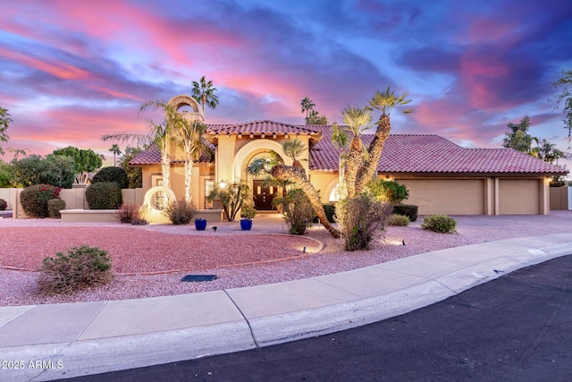 mediterranean / spanish home featuring driveway, an attached garage, a tiled roof, and stucco siding