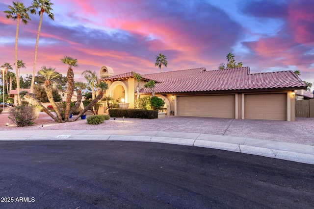 mediterranean / spanish-style house featuring driveway, a tiled roof, an attached garage, and stucco siding