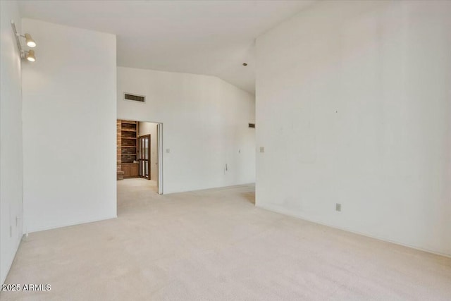 spare room featuring light carpet, vaulted ceiling, and visible vents