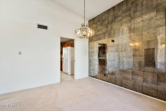 unfurnished room featuring light carpet, a high ceiling, visible vents, and an inviting chandelier