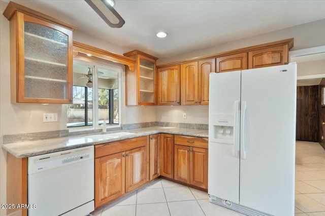 kitchen featuring light stone countertops, white appliances, a sink, brown cabinets, and glass insert cabinets