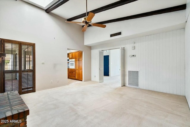 empty room featuring light carpet, a ceiling fan, visible vents, and beamed ceiling