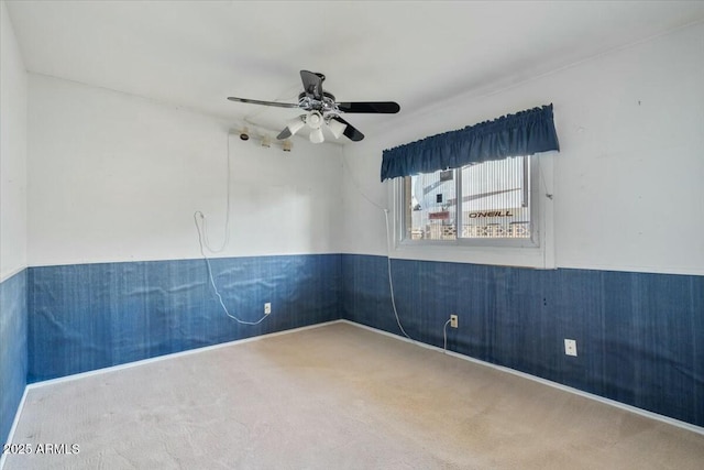 unfurnished room featuring a wainscoted wall, ceiling fan, and carpet