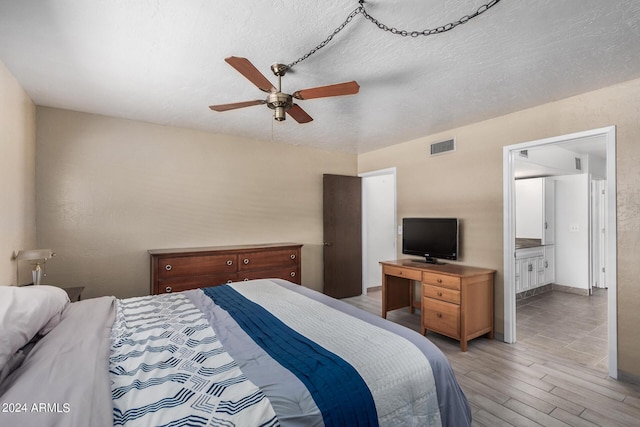 bedroom with visible vents, baseboards, ensuite bath, a textured ceiling, and light wood-style floors