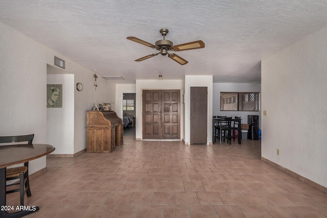 living room with a ceiling fan, visible vents, a textured ceiling, and a textured wall