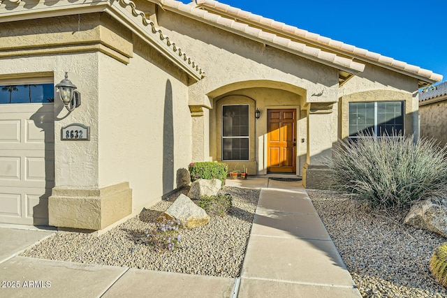 doorway to property featuring a garage, a tiled roof, and stucco siding