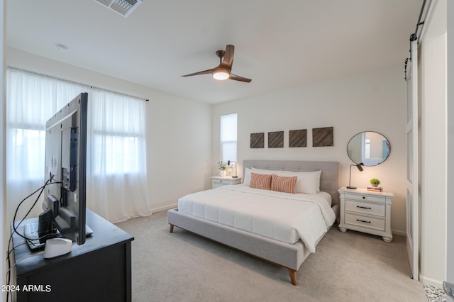 bedroom featuring light carpet, visible vents, ceiling fan, and a barn door