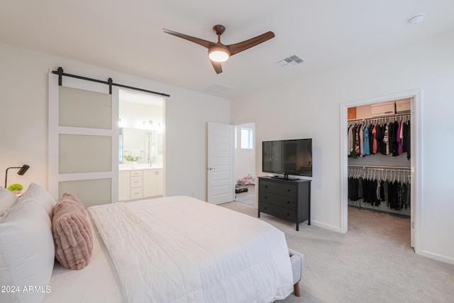 bedroom with visible vents, a closet, light carpet, a walk in closet, and a barn door