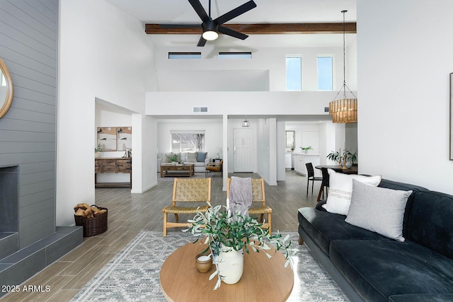 living room with beamed ceiling, wood-type flooring, a large fireplace, and ceiling fan