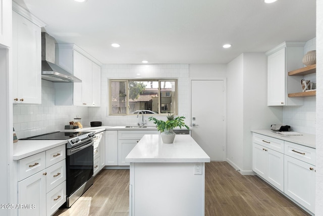 kitchen featuring hardwood / wood-style floors, white cabinetry, sink, stainless steel range with electric stovetop, and wall chimney range hood