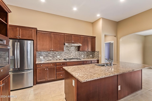 kitchen featuring sink, light stone counters, backsplash, an island with sink, and appliances with stainless steel finishes