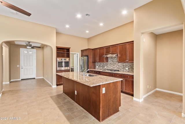 kitchen featuring a center island with sink, sink, ceiling fan, light stone countertops, and appliances with stainless steel finishes