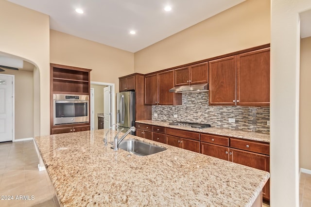 kitchen with sink, decorative backsplash, an island with sink, appliances with stainless steel finishes, and light stone counters