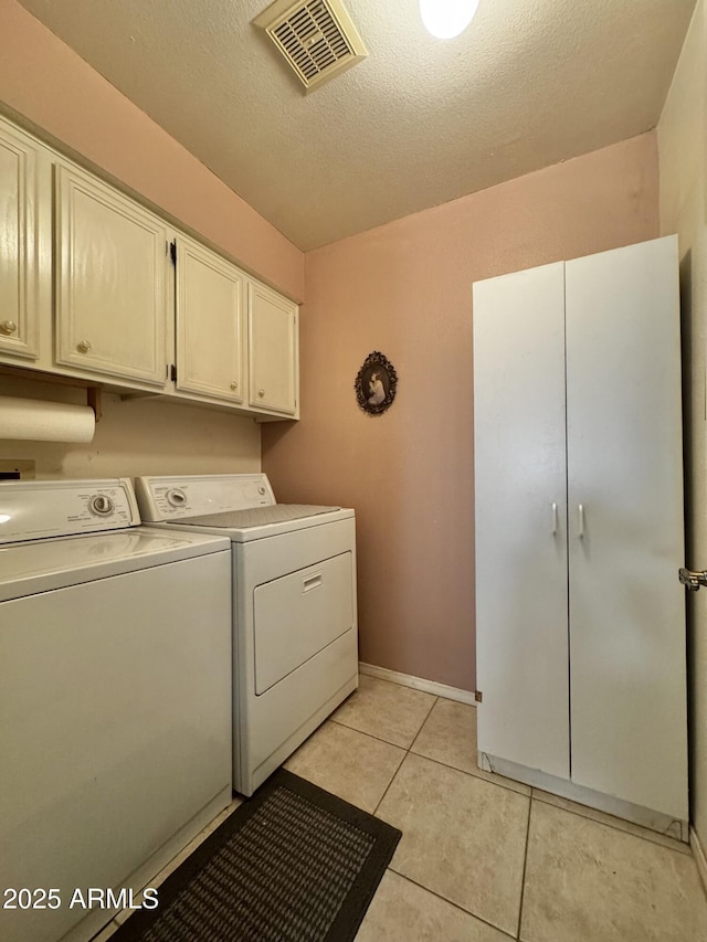 washroom featuring light tile patterned floors, a textured ceiling, washing machine and dryer, visible vents, and cabinet space