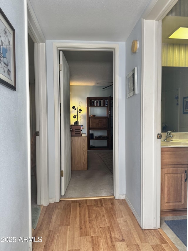 hall featuring light wood-type flooring, baseboards, and a sink