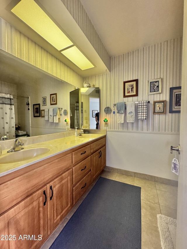 bathroom with double vanity, tile patterned flooring, a sink, and wallpapered walls