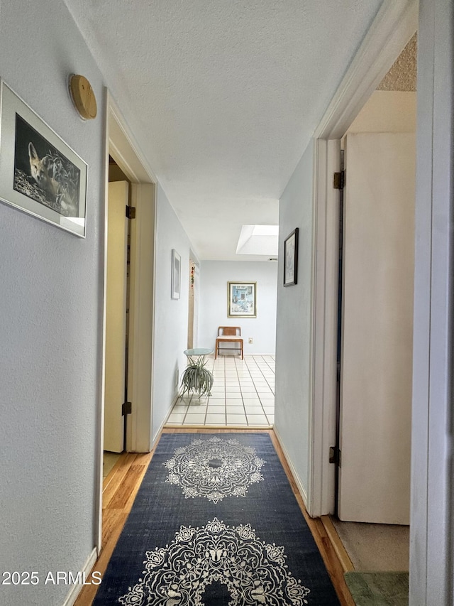 hallway featuring a skylight, a textured wall, a textured ceiling, wood finished floors, and baseboards