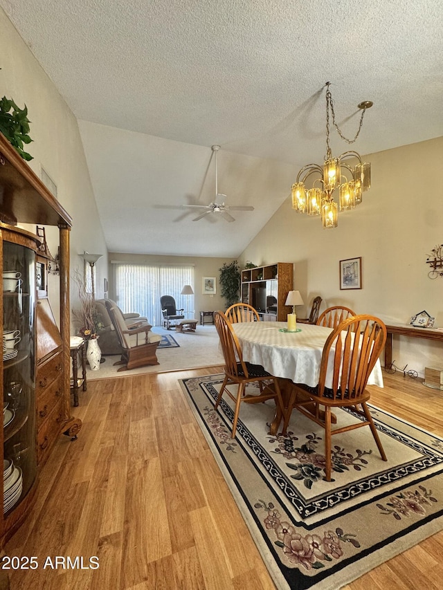 dining space with lofted ceiling, light wood-style flooring, and a textured ceiling