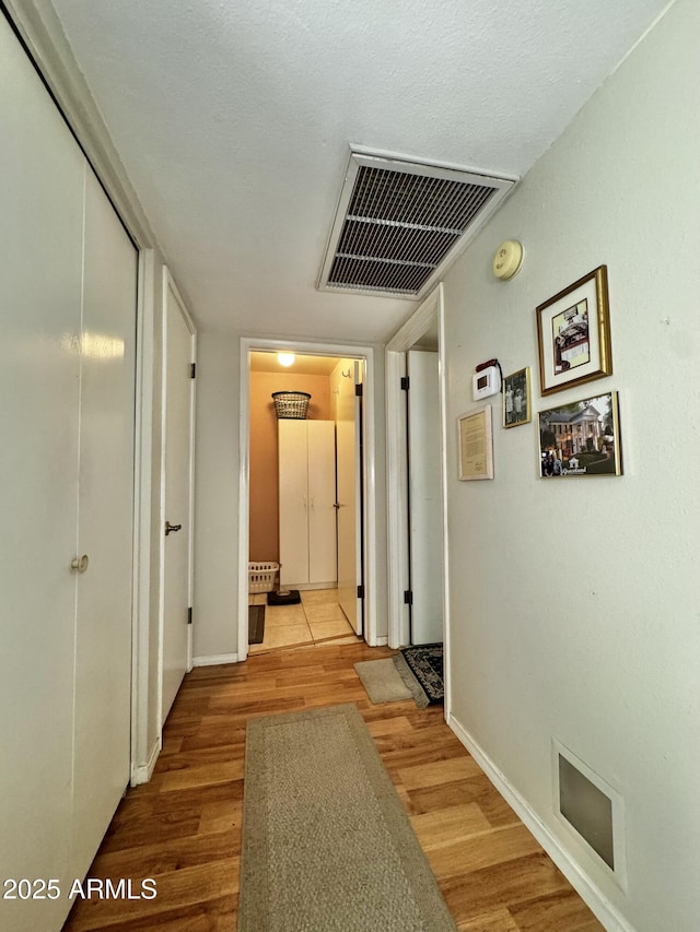 hallway with visible vents, baseboards, and wood finished floors