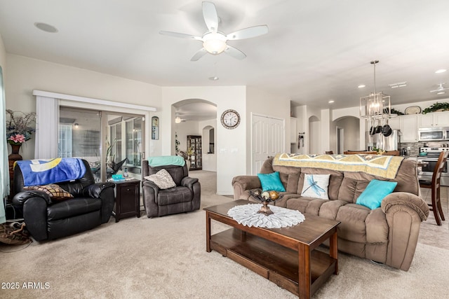 carpeted living room with ceiling fan with notable chandelier