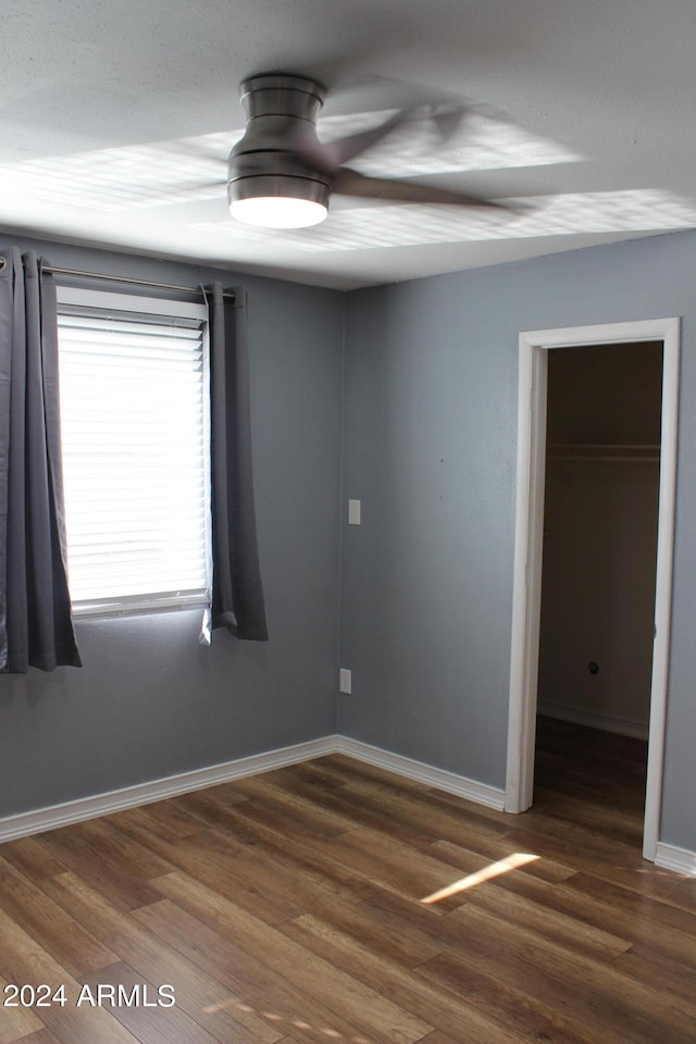 unfurnished bedroom with ceiling fan, a closet, dark hardwood / wood-style flooring, and a walk in closet