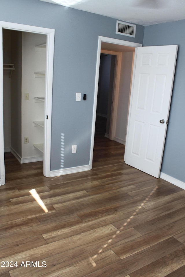 unfurnished bedroom with a closet, a walk in closet, and dark hardwood / wood-style floors