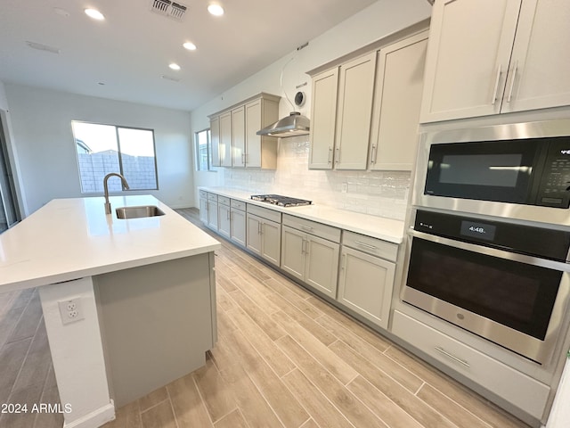 kitchen featuring gray cabinets, an island with sink, appliances with stainless steel finishes, tasteful backsplash, and sink