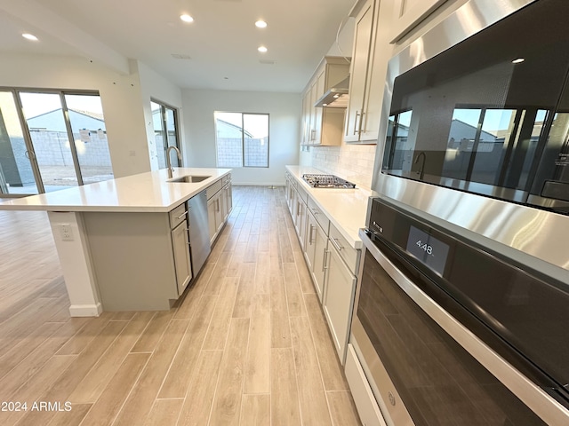 kitchen featuring tasteful backsplash, sink, light hardwood / wood-style flooring, appliances with stainless steel finishes, and an island with sink