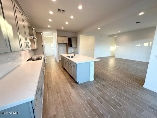 kitchen featuring stainless steel gas stovetop, decorative backsplash, wood-type flooring, sink, and a kitchen island with sink