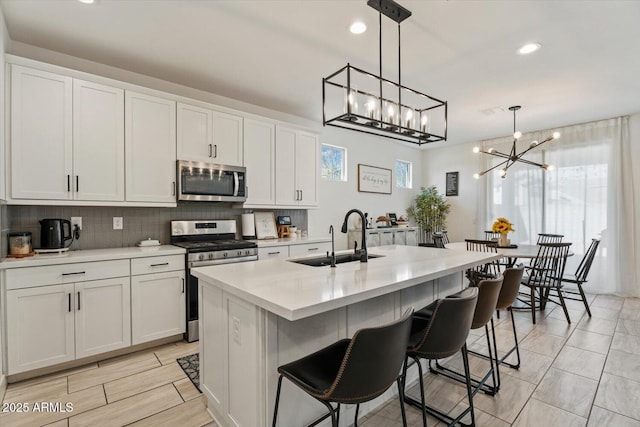 kitchen featuring hanging light fixtures, stainless steel appliances, white cabinets, and a center island with sink