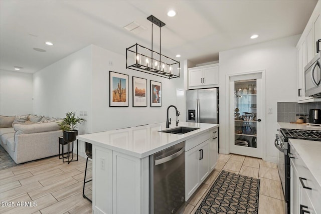 kitchen featuring sink, an island with sink, pendant lighting, stainless steel appliances, and white cabinets