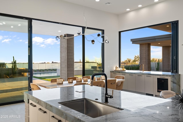 kitchen featuring stone countertops, beverage cooler, a sink, a healthy amount of sunlight, and white cabinets