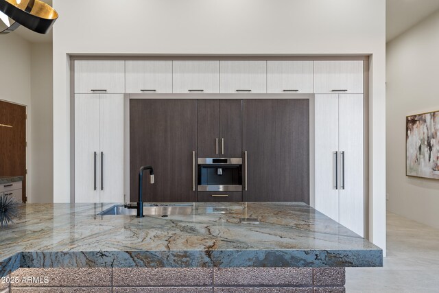 kitchen featuring light stone countertops, a sink, stainless steel oven, and white cabinetry